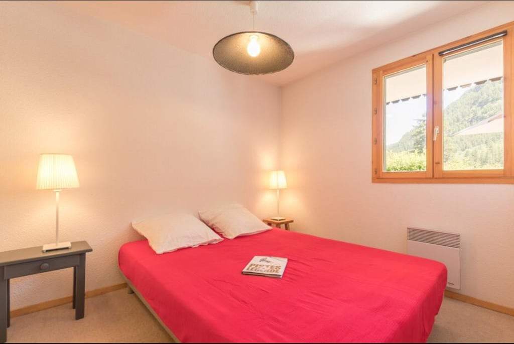 Chambre avec lit double, lampes de chevet et fenêtre ouvrant sur la forêt de mélèzes