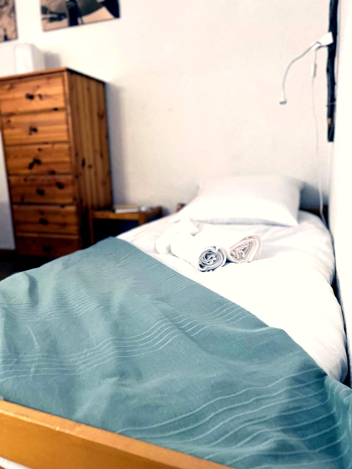 Lit simple avec plaid vert d’eau et commode en bois dans une chambre de l’appartement à Serre Chevalier