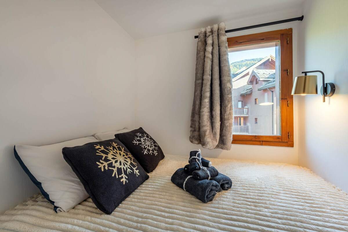 Coin nuit avec lit double, coussins flocons brodés, rideau en fausse fourrure et applique en laiton, vue sur les chalets
