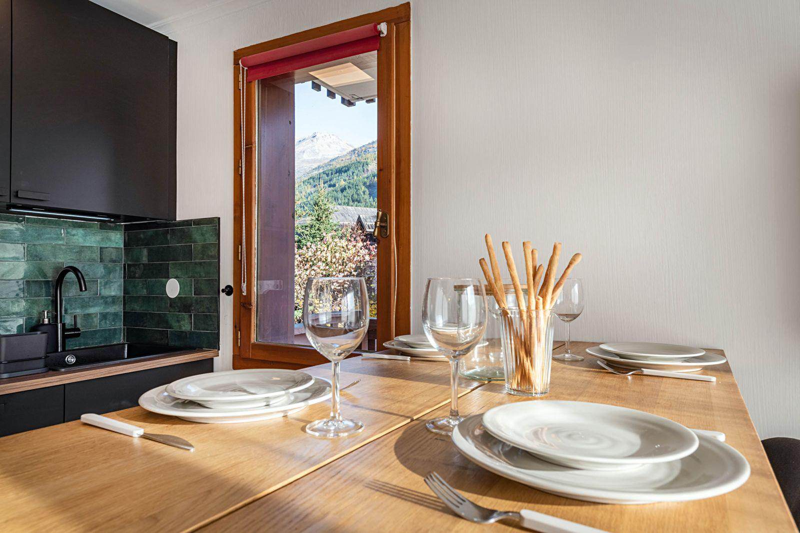 Table dressée dans la cuisine d'un logement à Briançon avec vue sur la montagne par la fenêtre, prêt pour un dîner par chef privé