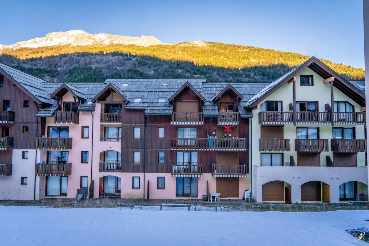 Façade de la résidence du Flocon au soleil couchant, balcons de bois et sommet enneigé en arrière-plan