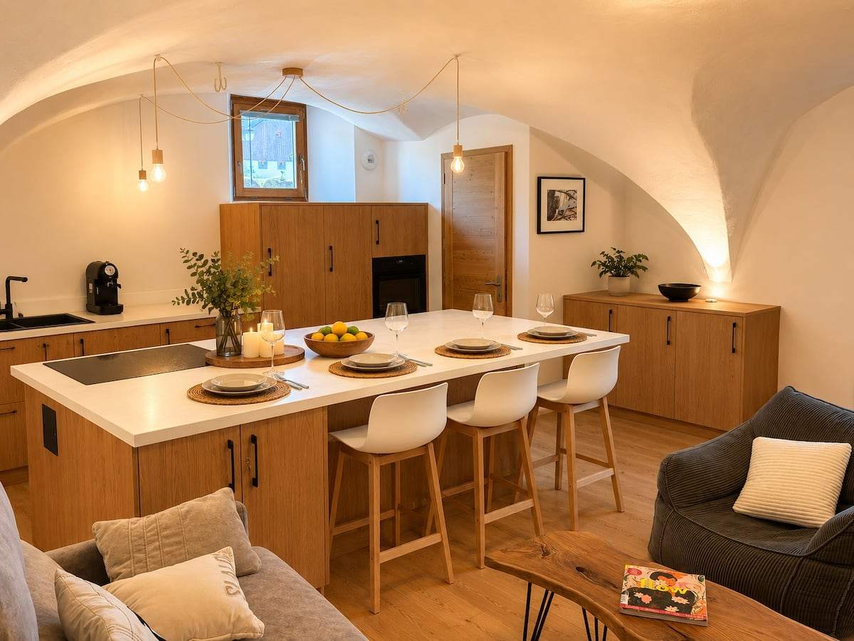Îlot de cuisine en chêne sous les voûtes, tabourets blancs, ampoules suspendues et table dressée