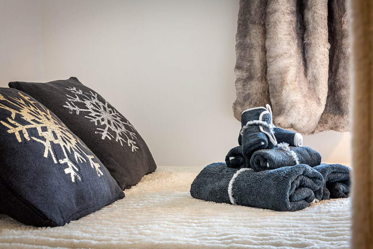 Linge de bain roulé et coussins flocons posés sur le lit, plaid en fausse fourrure