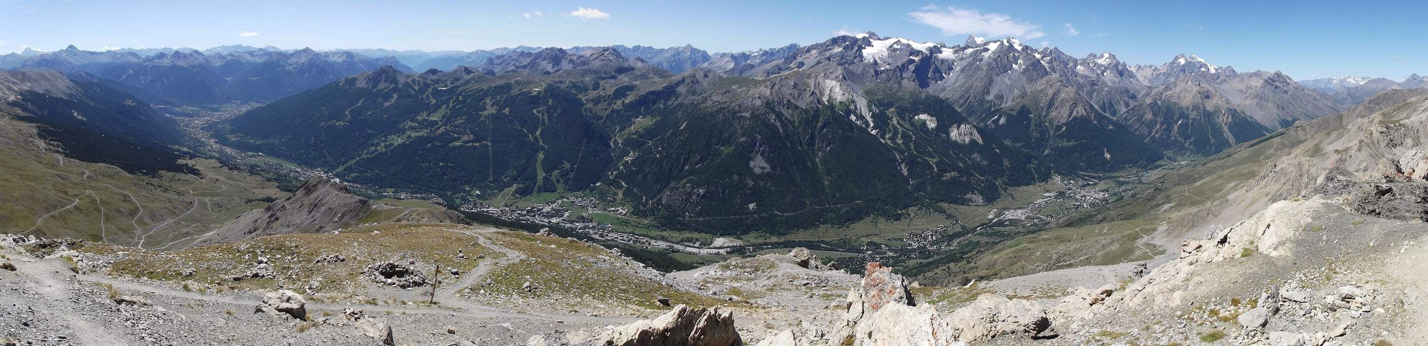 Panorama de la vallée de la Guisane depuis le sommet du Grand Aréa : villages de Serre Chevalier alignés au fond de vallée, versant boisé du domaine skiable et sommets du massif des Écrins