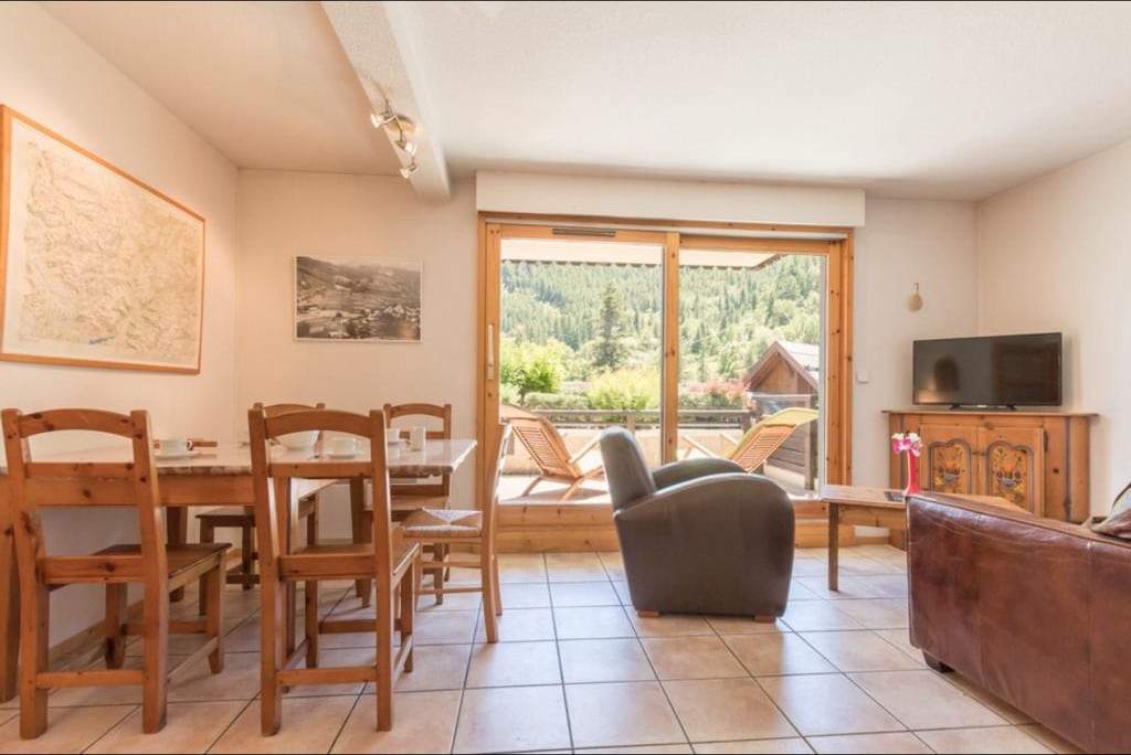 Séjour de l'appartement avec table à manger en bois, fauteuil, canapé en cuir et grande baie vitrée ouvrant sur la terrasse