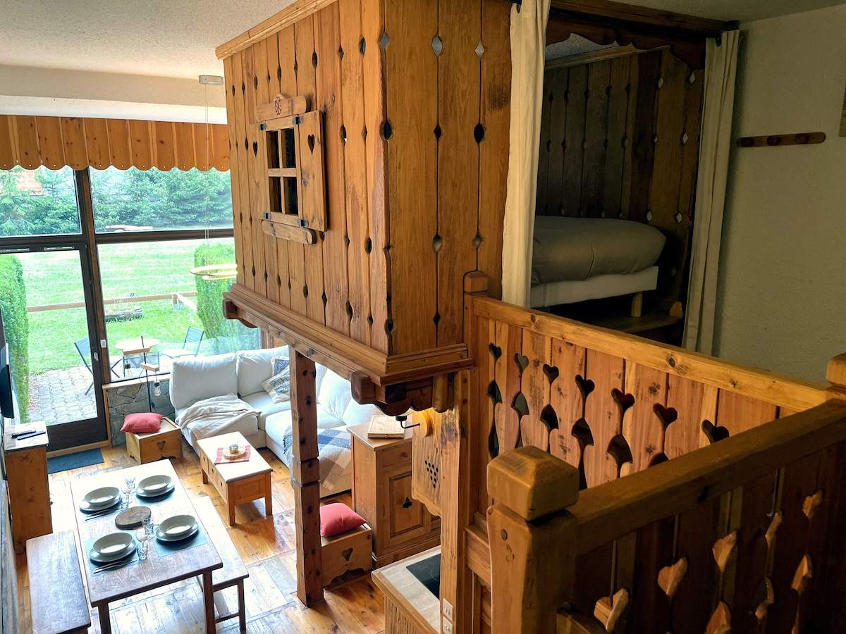 Vue d'ensemble du séjour de l'appartement à Serre Chevalier avec la cabane en bois sculptée en surplomb et le jardin en arrière-plan