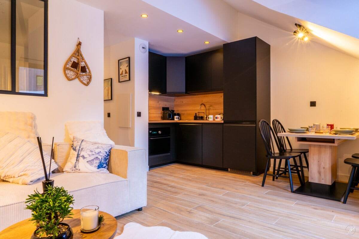 Cuisine noire mate avec crédence en bois, four, plaques et table haute, ouverte sur le salon