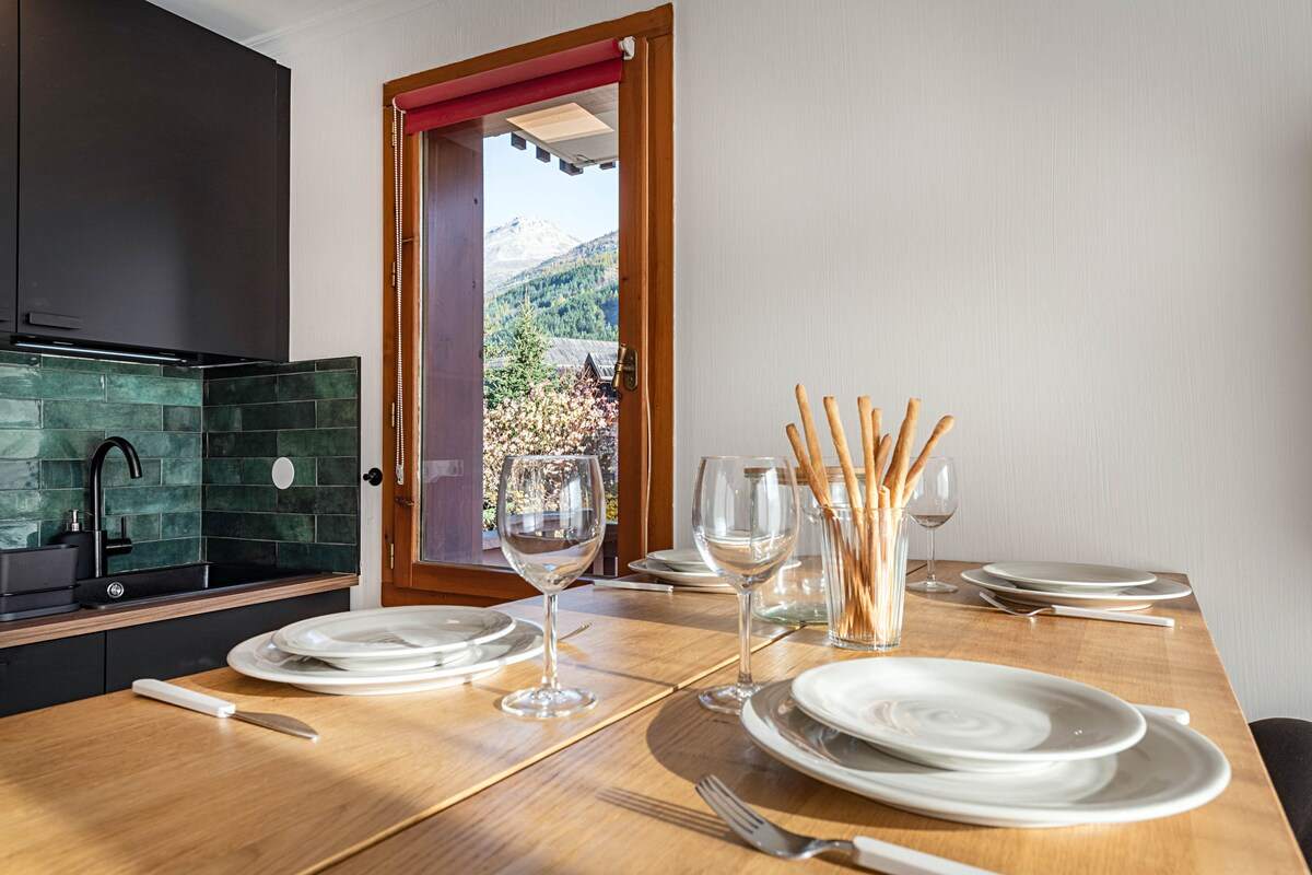 Table dressée pour quatre avec vue sur les sommets par la fenêtre, verres à vin et gressins