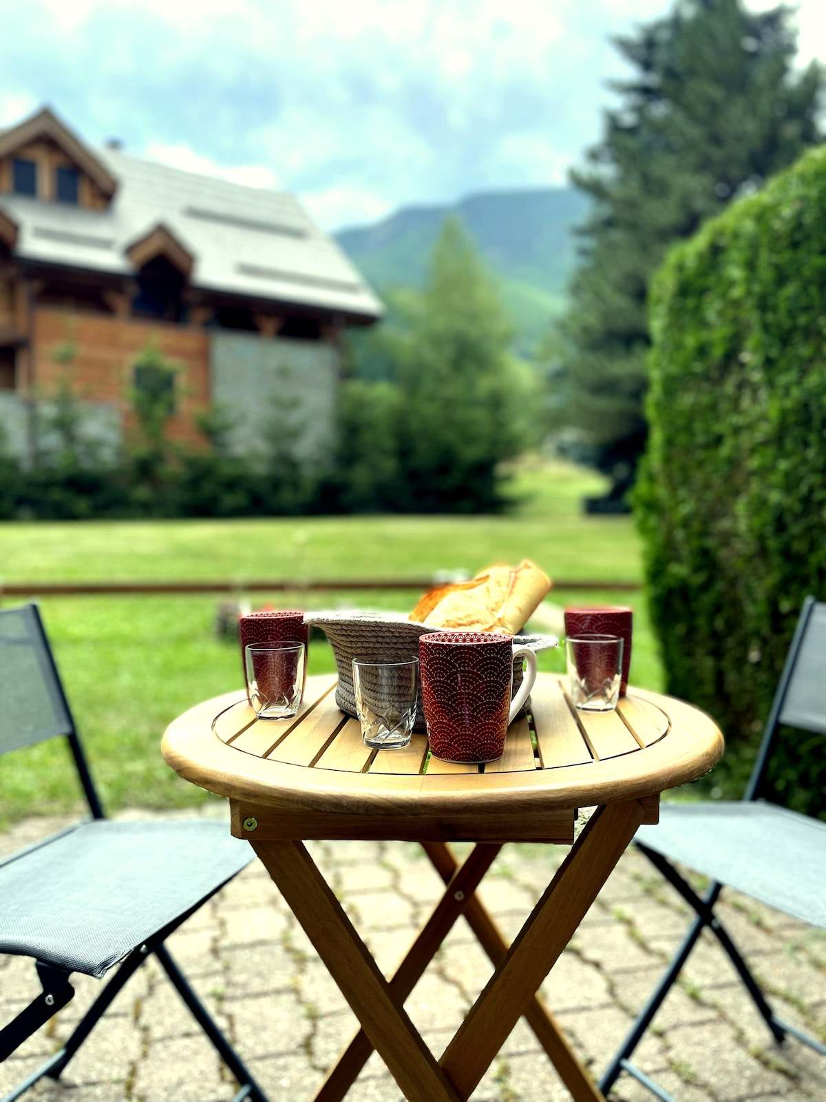 Petit-déjeuner servi sur la table de la terrasse-jardin de l'appartement à Serre Chevalier, vue sur les montagnes et la pelouse