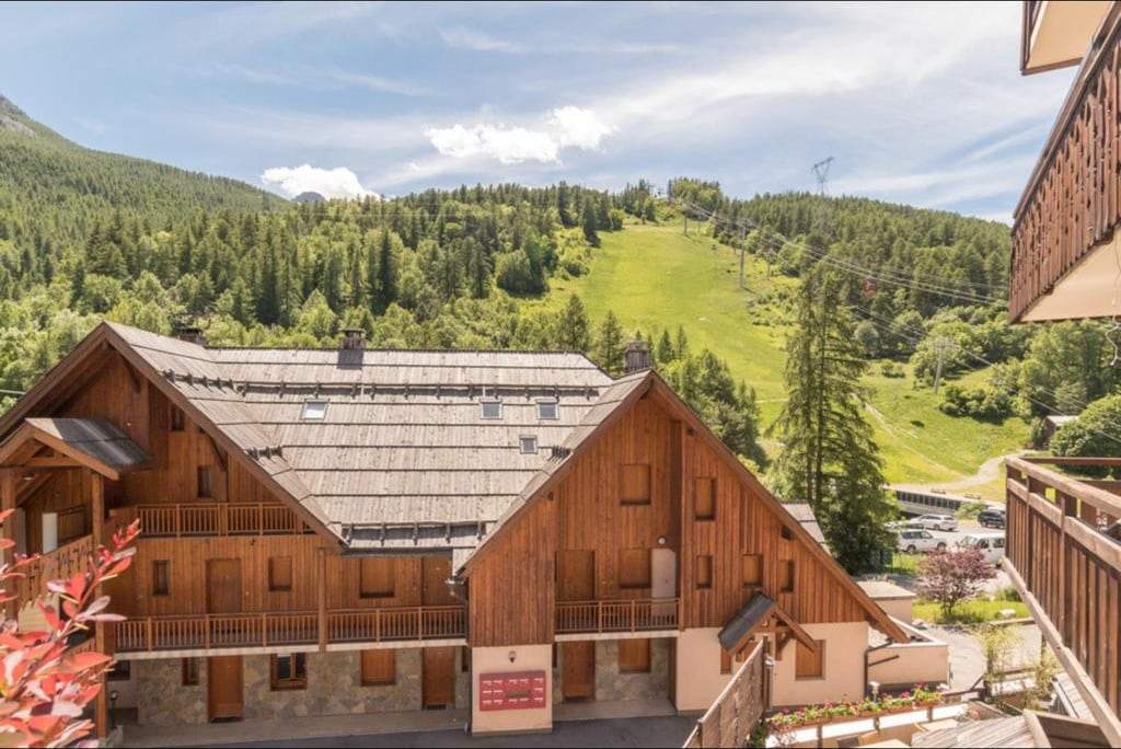 Vue depuis le balcon sur les chalets voisins, le télésiège et le versant vert du domaine en été